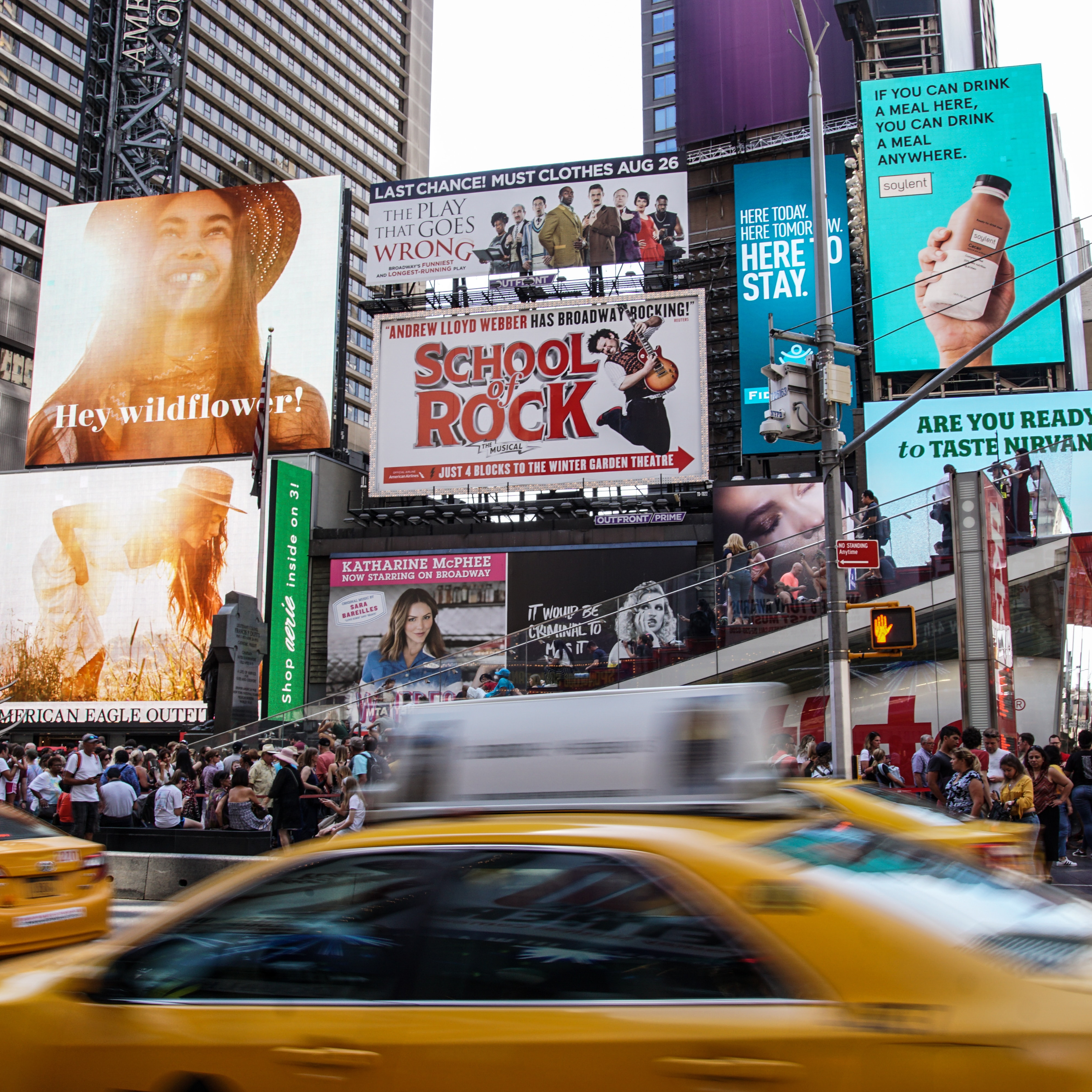 Große Werbefläschen am New York Times Square mit Menschenmassen und zwei vorbeifahrenden Taxis