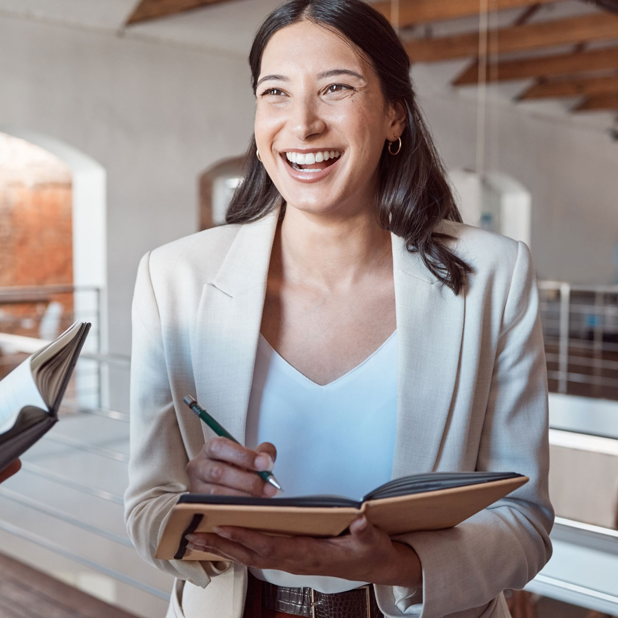Junge Frau macht sich während der Arbeit Notizen in ein Buch und lacht