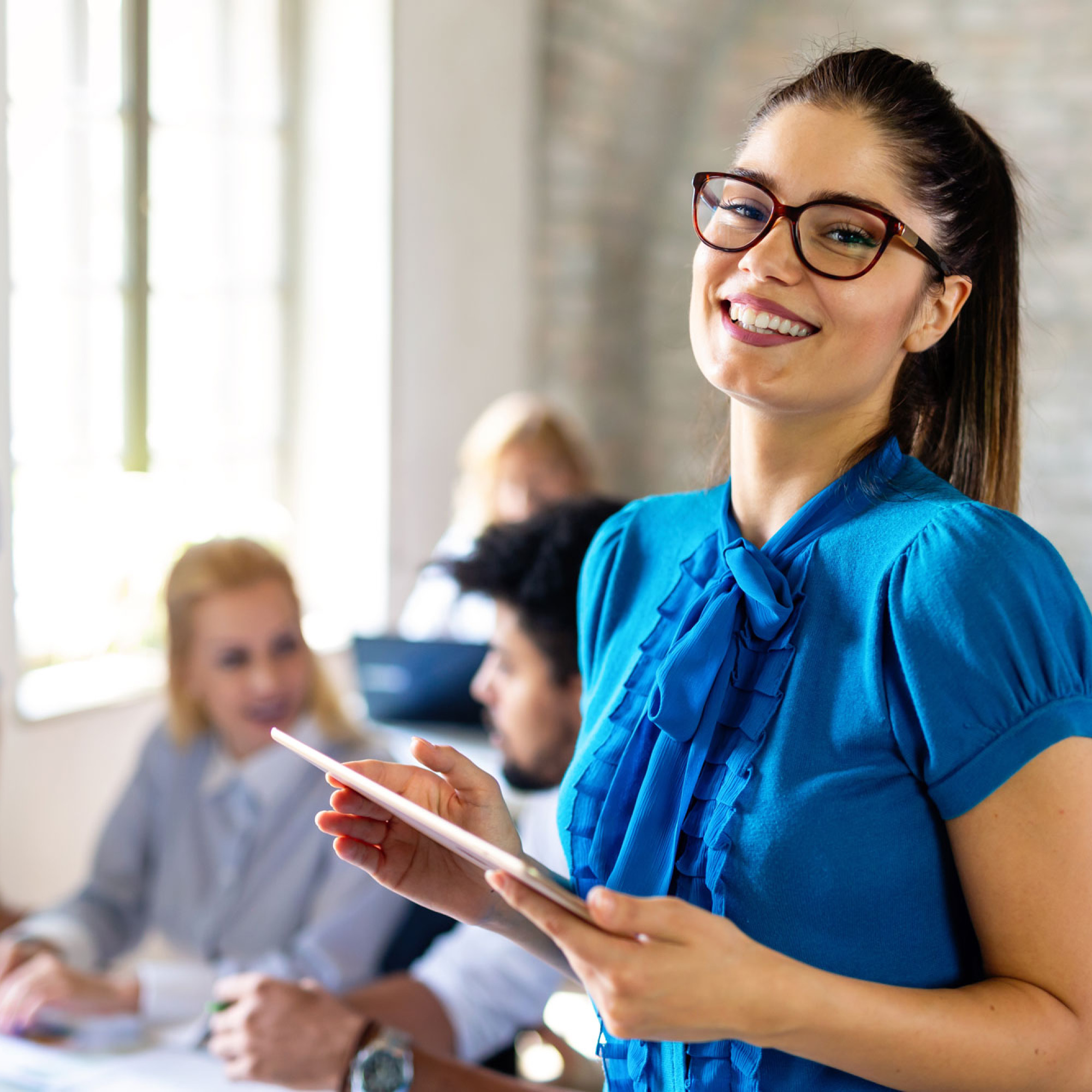 Studentin des MBA Projekt- und Prozessmanagement steht in einem Meeting mit Arbeitskollegen mit einem Ipad in der Hand